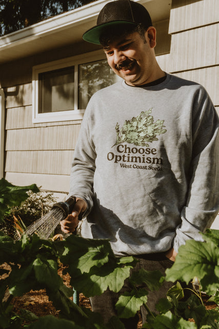 a guy watering plants with our choose optimism garden wear