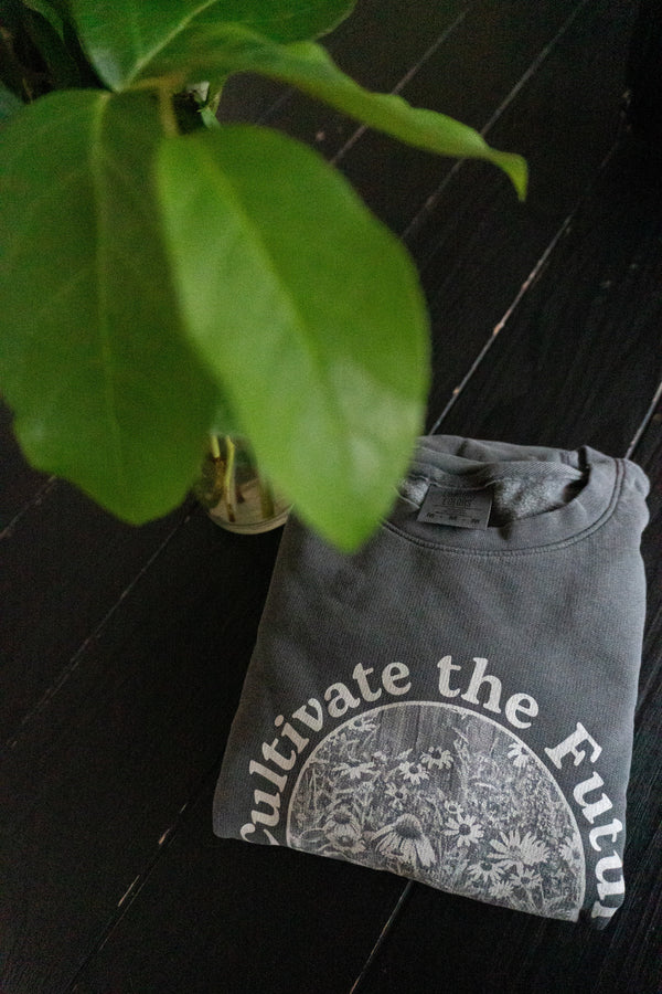 Cultivate the future sweatshirt folded on table with a plant