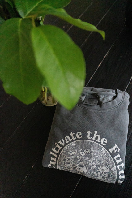 Cultivate the future sweatshirt folded on table with a plant