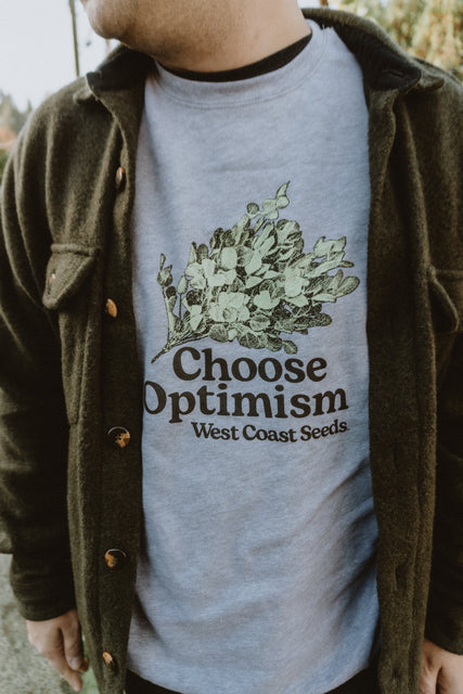 A person wearing choose optimism sweatshirt west coast seeds beneath an overshirt