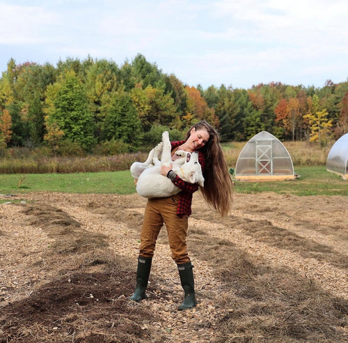 Amber holding a white dog standing in her garden surrounded by nature